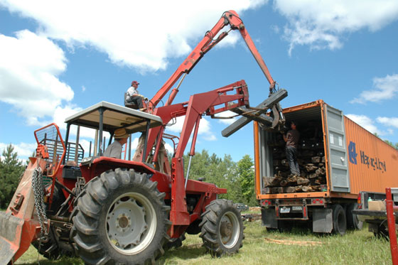 Tractor and clam loader loading square logs into container